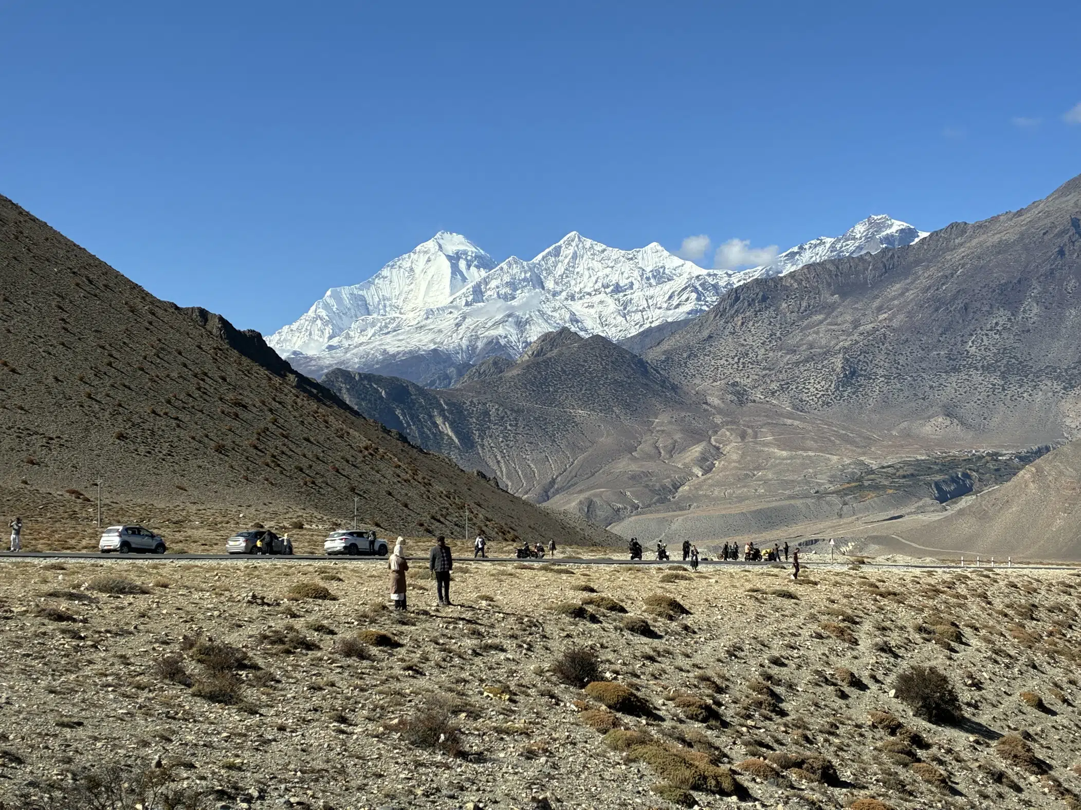 Trekkers crossing the rugged landscape beneath snow-capped mountains in Upper Mustang